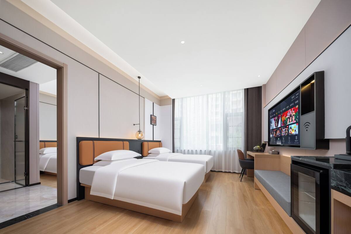 A modern hotel room with a large bed, a desk, a TV, and a view of the city.