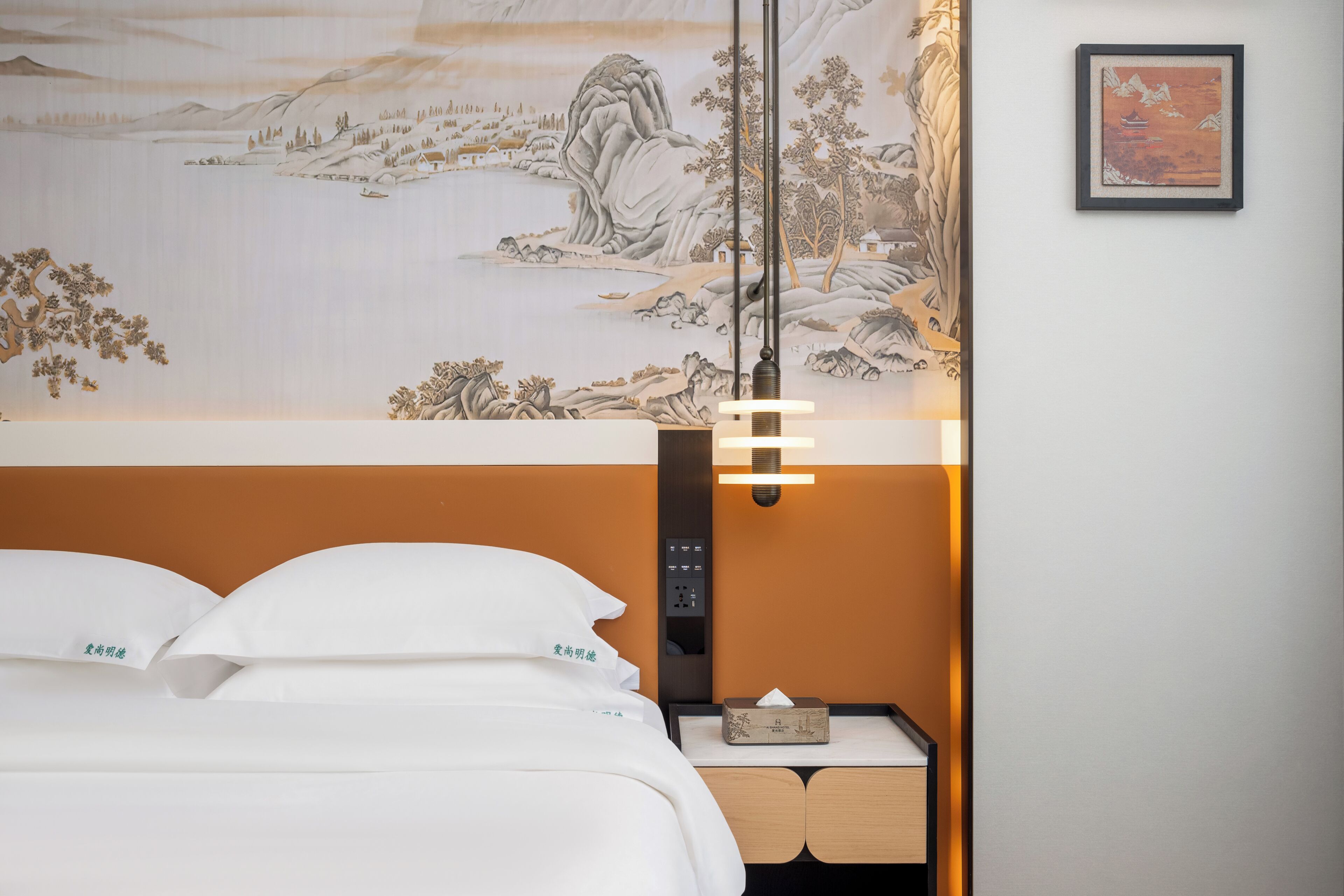 Habitación de hotel con cama, mesita de noche, lámpara de pared y un cuadro.