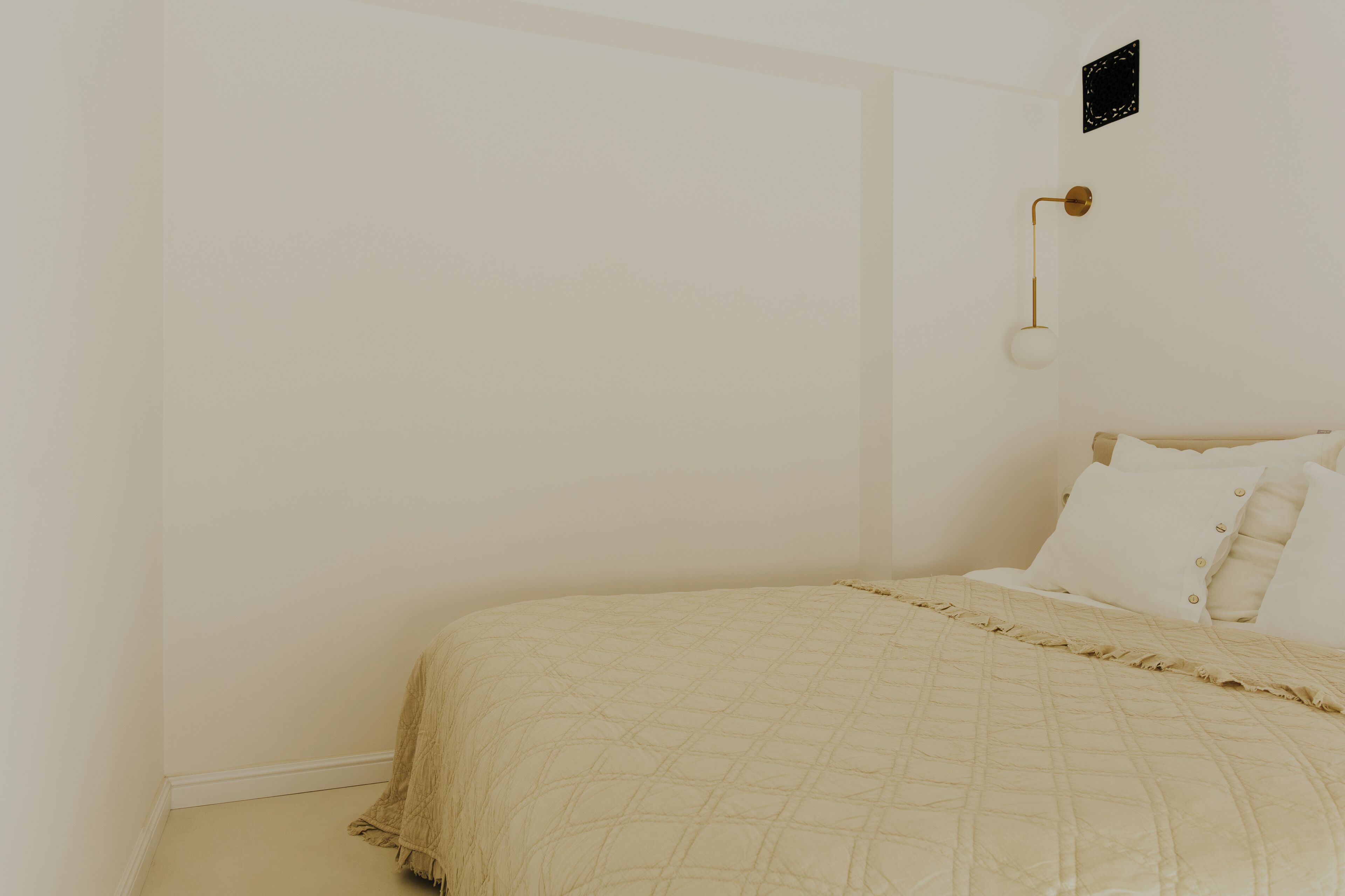 A bedroom with a bed, a wall-mounted light fixture, and a small wall decoration.
