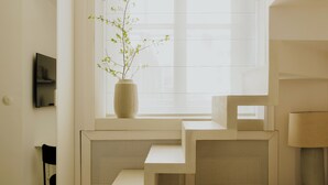 A modern room with a window, a vase with a plant, a small table, and a bed. - N46 Studio Apartment  (Warsaw)