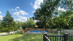 Ein Garten mit Schwimmbad, einer Holzterrasse und einem eingezäunten Bereich.