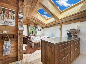 A rustic interior with wooden beams, a skylight, a sofa, a coffee table, and a kitchen area. - Matterhorn Alpine Hideaway - Cozy Renovated Apartm (Zermatt)