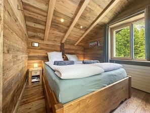 A wooden cabin bedroom with a bed, bedside table, and a window with a view of trees. - Matterhorn Alpine Hideaway - Cozy Renovated Apartm (Zermatt)