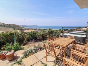Un patio al aire libre con una mesa y sillas de madera, un jacuzzi y vistas al mar.