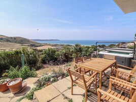 Un patio al aire libre con una mesa y sillas de madera, un jacuzzi y vistas al mar.