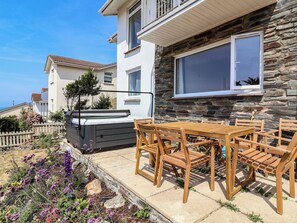 Ein Wohnhaus mit Steinaußenwand, einer Terrasse mit Holzmöbeln und einem Garten mit violetten Blumen.
