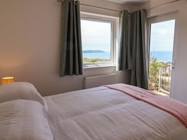 Un dormitorio con cama, ventana con cortinas, radiador y vista al mar.
