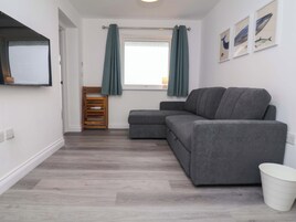 Una sala moderna con un sofá seccional gris, una silla de madera, un cesto de basura blanco y una ventana con cortinas.
