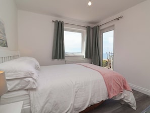 A bedroom with a bed, a window with curtains, a radiator, and a view of the outdoors. - Belvedere (Woolacombe)