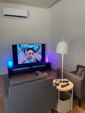 A living room with a TV, a lamp, and a gaming setup. - Diker Port Residence (9) Mobilyalı ve Denize 5 Dk (konyaaltı)