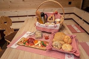 A wooden table with a checkered tablecloth, a basket with bread and condiments, and a wooden chair. - Parndlehof Room Engel with Mountain View, Shared Terrace and Wi-Fi (Villanders)