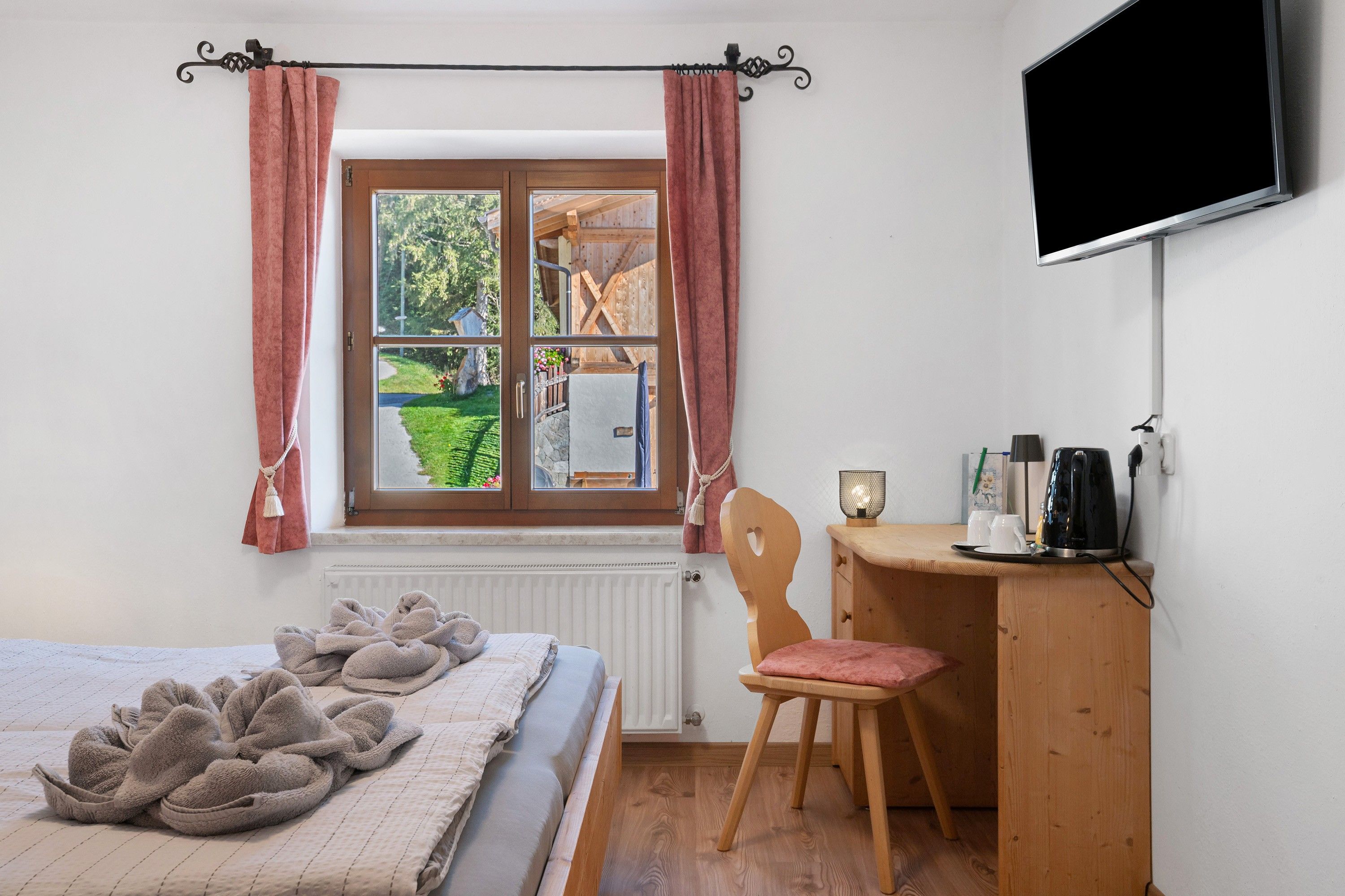 Un dormitorio con una cama, un escritorio de madera, una silla, un televisor y una ventana con cortinas.