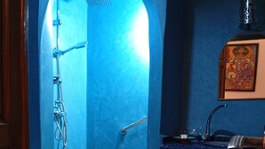 Un baño con pared azul, ducha, lavabo y una toalla en el suelo.