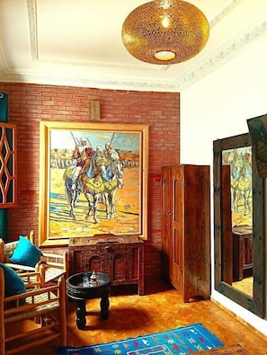 Une pièce comprenant un grand tableau représentant une scène de bataille historique, un meuble en bois, une petite table avec une bougie et un tapis à motifs.