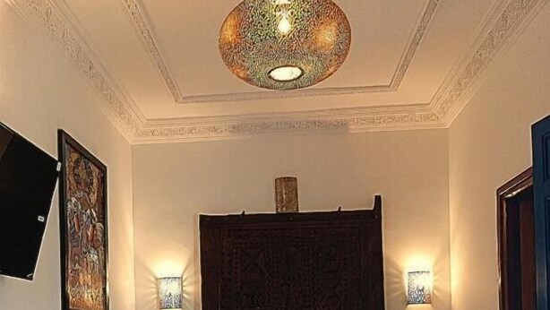 Un dormitorio con una cama grande, dos lámparas de noche, una lámpara decorativa en el techo y un televisor montado en la pared.