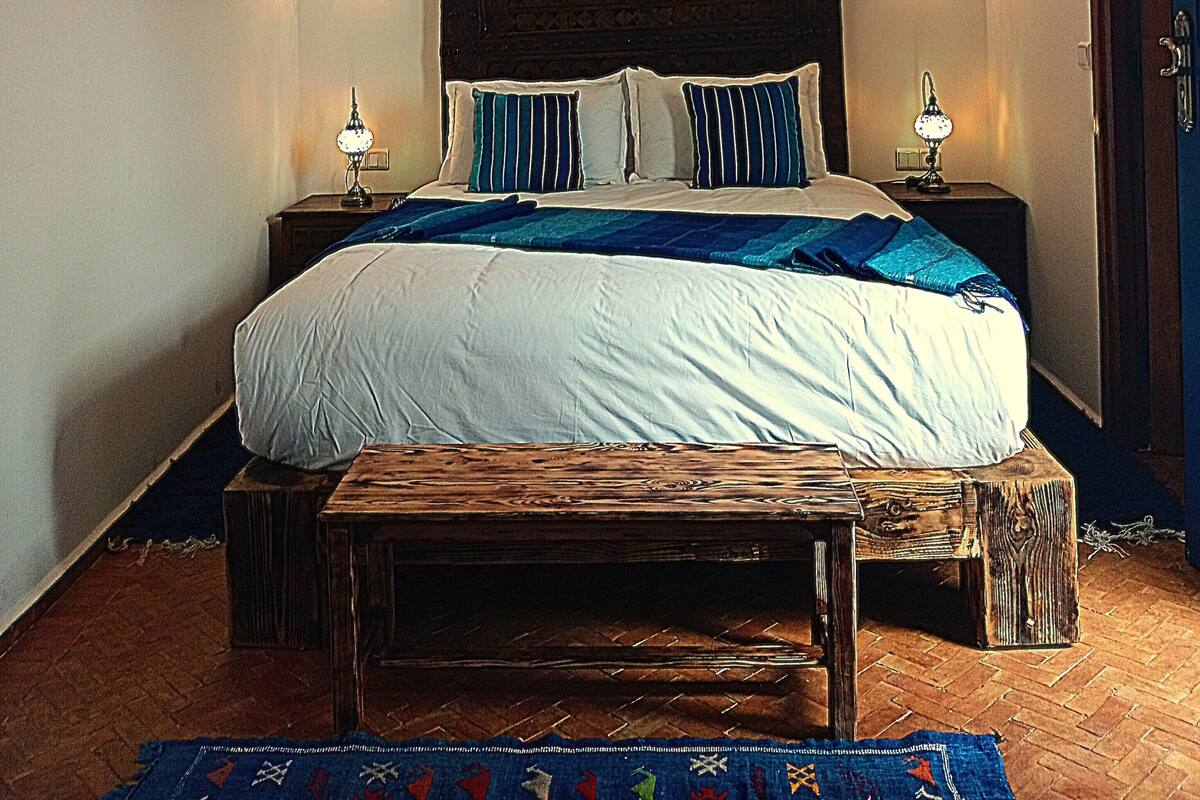 Un dormitorio con una cama grande, dos lámparas de noche, una lámpara decorativa en el techo y un televisor en la pared.