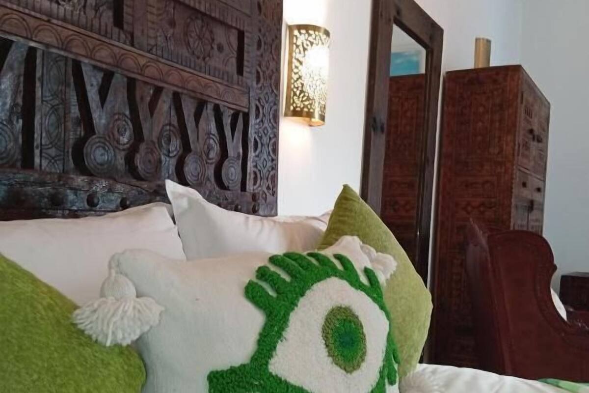 Una cama con un cojín verde y blanco, un cabecero de madera y un espejo.
