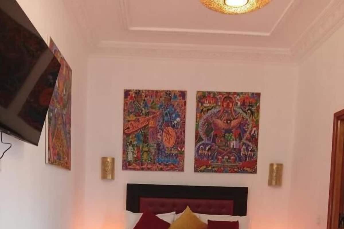 Un dormitorio con una cama, dos cuadros en la pared, lámparas de noche y un banco de madera.
