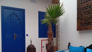 Una habitación con una cama, una mesa con comida, una palmera y puertas azules.