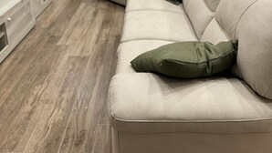 Een moderne woonkamer met een beige bank, een houten kast, een potplant en een deur die naar een andere kamer leidt.
