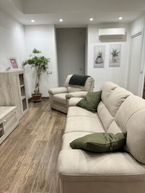 A modern living room with a beige sofa, a wooden cabinet, a potted plant, and a door leading to another room. - The Mox Luxury Apartament (Napoli)