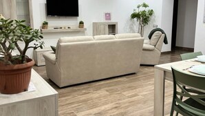 Een moderne woonkamer met een bank, een televisie, een eettafel en een potplant.
