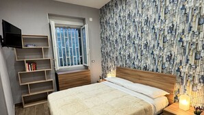 Een slaapkamer met een bed, een televisie, een raam en een behang met patroon.
