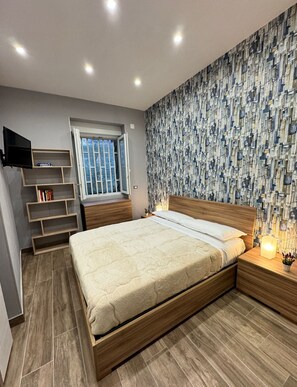 A bedroom with a bed, a TV, a window, and a patterned wall. - The Mox Luxury Apartament (Napoli)