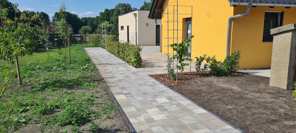 A pathway leading to a yellow building with a garden area on one side.