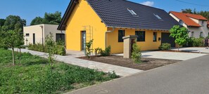 A yellow house with a dark roof, a satellite dish, and a small garden area.