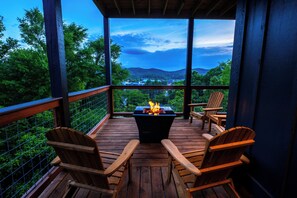Un terrazzo in legno con un braciere, sedie e vista su una città e montagne.