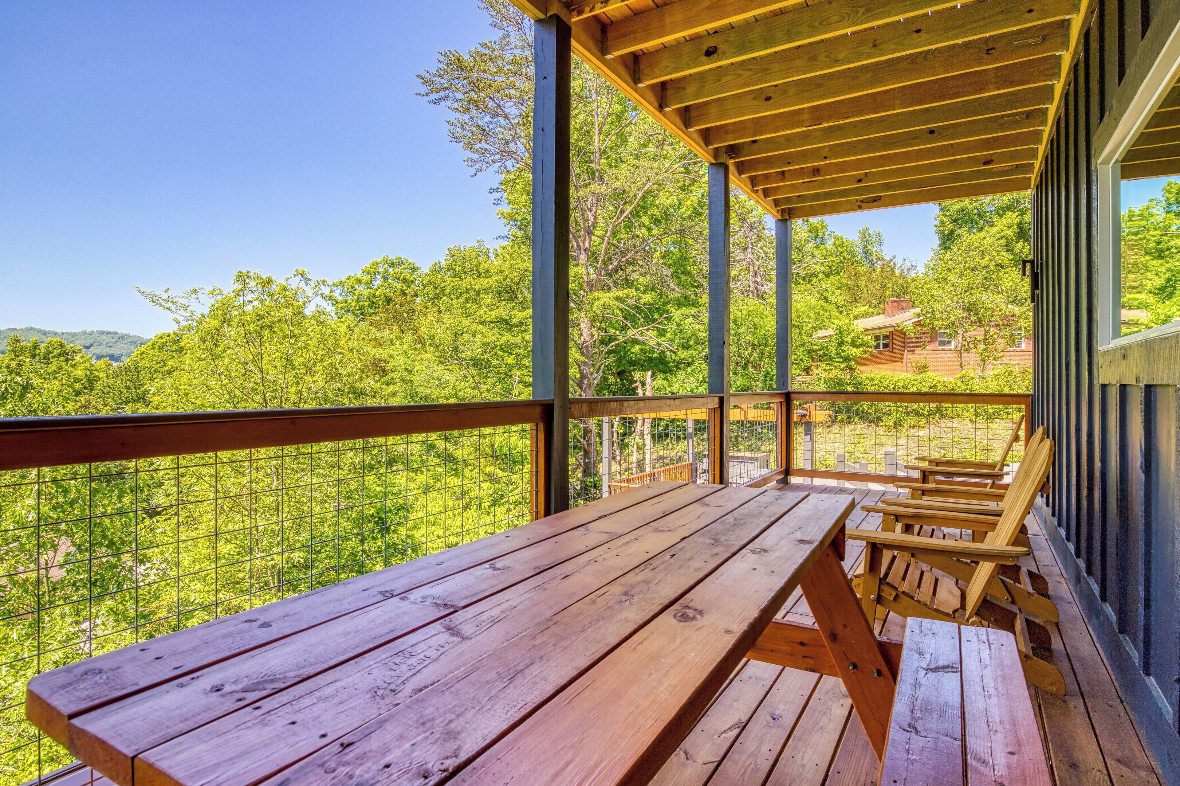 Una terraza de madera con una mesa y sillas, con vistas a un paisaje verde y un edificio a lo lejos.