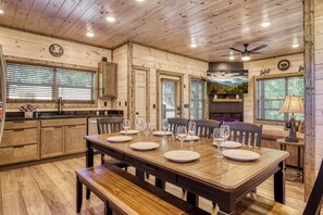 Un interior de madera con una mesa de comedor para cuatro personas, una zona de cocina y un ventilador de techo.