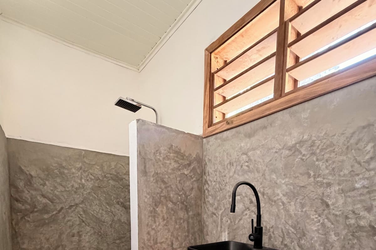 A bathroom with a shower, a black sink on a wooden shelf, and a textured wall.