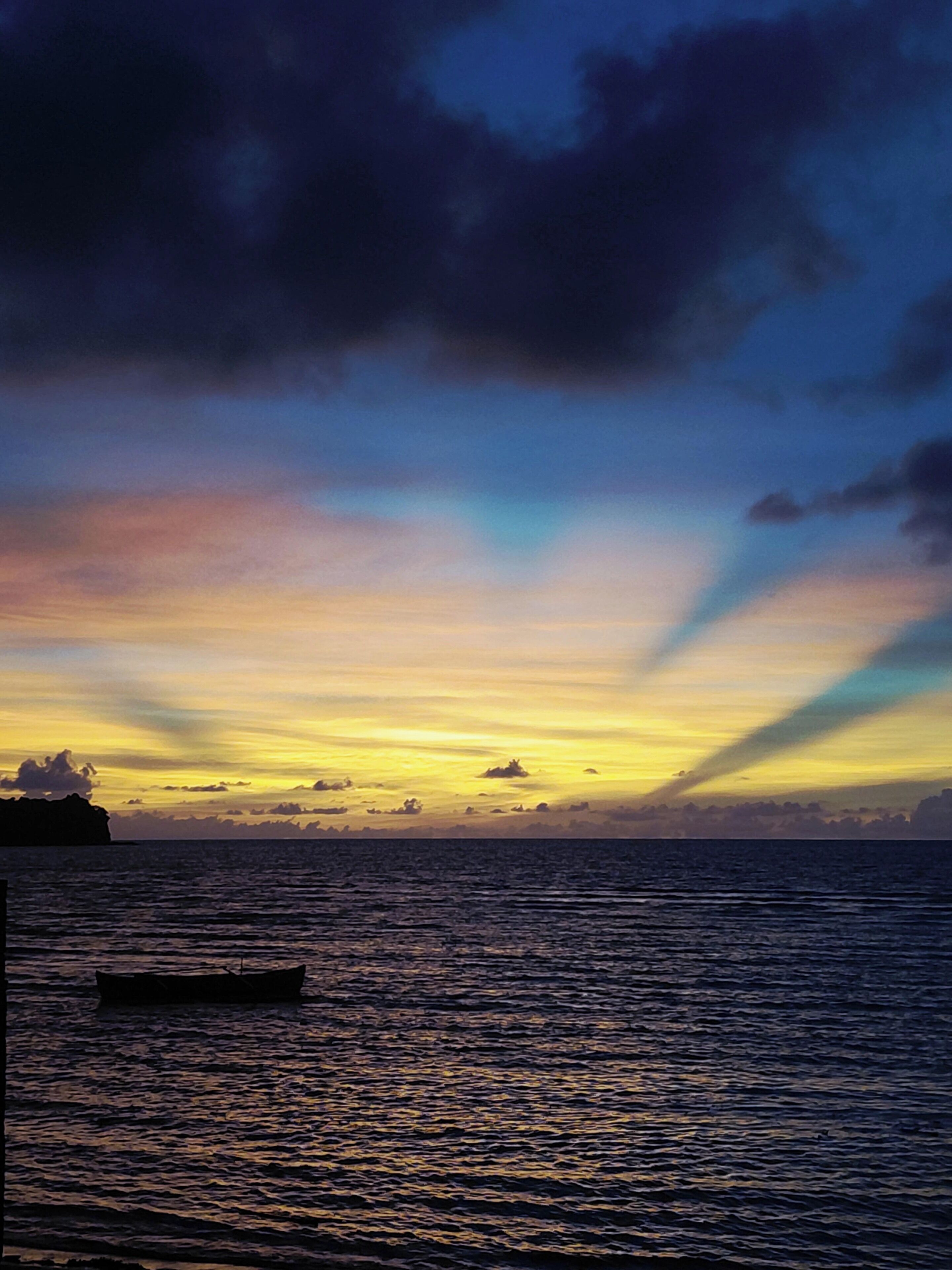Un atardecer sobre un mar tranquilo con un barco y tierra a lo lejos.