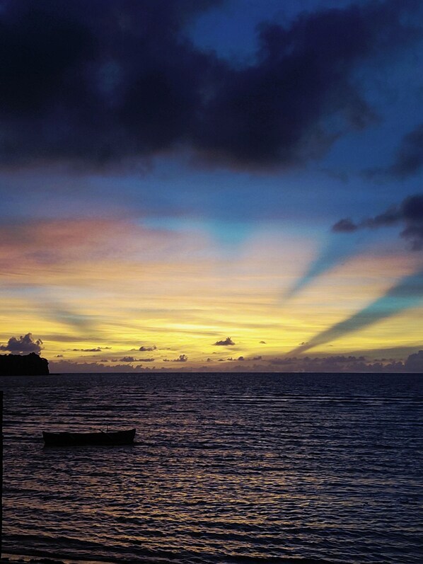 Un coucher de soleil sur une mer calme, avec un bateau et une terre lointaine à l'horizon.