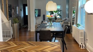 Een moderne keuken met een visgraatvloer, een eethoek met een grote tafel, en een woonkamer met een bank en een televisie.