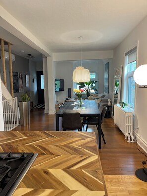Une cuisine moderne avec un parquet en chevrons, un coin repas doté d’une grande table et un salon avec un canapé et un téléviseur.