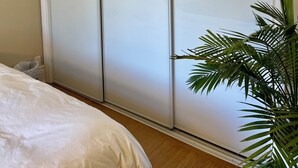 Een slaapkamer met een schuifdeurkast, een bed met witte lakens en een kamerplant.