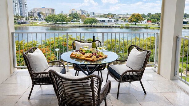 Un balcon avec une table dressée pour un repas, des chaises en osier et une vue sur le paysage urbain et l’eau.