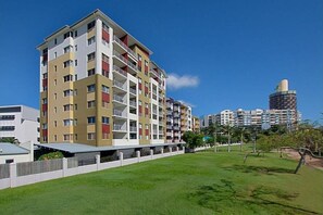 Ein mehrstöckiges Wohngebäude mit Balkonen, einer flachen Dachterrasse und einer Rasenfläche davor.