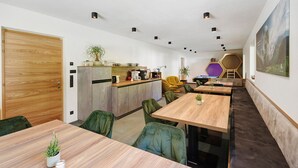 A modern interior with a wooden door, a kitchen area, a dining table with chairs, and a seating area with a sofa and a chair. - Family Apartment Nature House Bamboo – Lightness & Comfort with Mountain Views (Brennero)