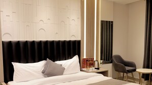 A modern hotel room with a large bed, a bedside table with a lamp, a chair, and a small table. - Hotel Boss In opposite New Delhi station (New Delhi)