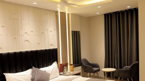 A modern hotel room with a large bed, a ceiling fan, a small table with chairs, and a large window with curtains. - Hotel Boss In opposite New Delhi station (New Delhi)