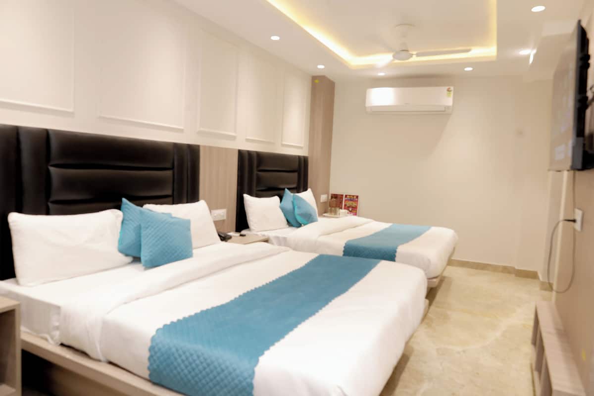 Una habitación de hotel con dos camas, un televisor de pantalla plana, un equipo de aire acondicionado y un ventilador de techo.