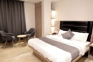 Camera d'albergo con un letto, due poltrone, un tavolino rotondo, un comodino con una lampada e un armadio.