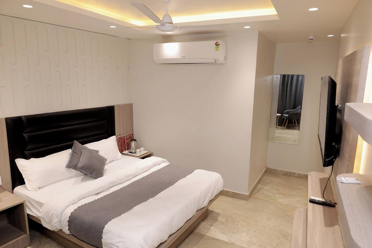 Una habitación de hotel moderna con una cama, mesita de noche, aire acondicionado, ventilador de techo, televisor y una ventana con cortinas.