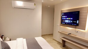 A hotel room with a bed, a TV mounted on the wall, a bedside table, and an air conditioning unit. - Hotel Boss In opposite New Delhi station (New Delhi)