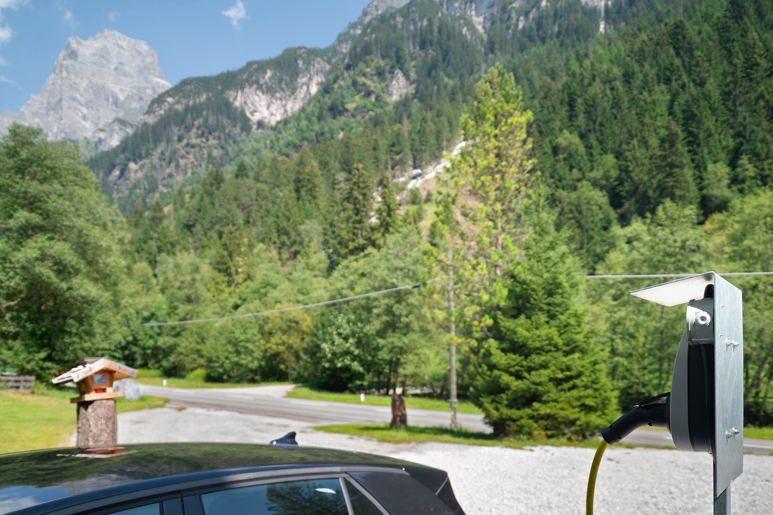 Ein Auto, geparkt in der Nähe einer solarbetriebenen Ladestation vor einer Bergkulisse.
