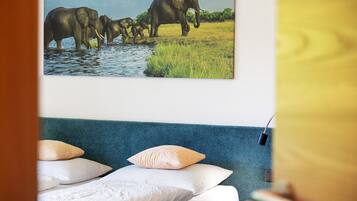 Een slaapkamer met een bed, kussens, een wandlamp en een schilderij van olifanten.